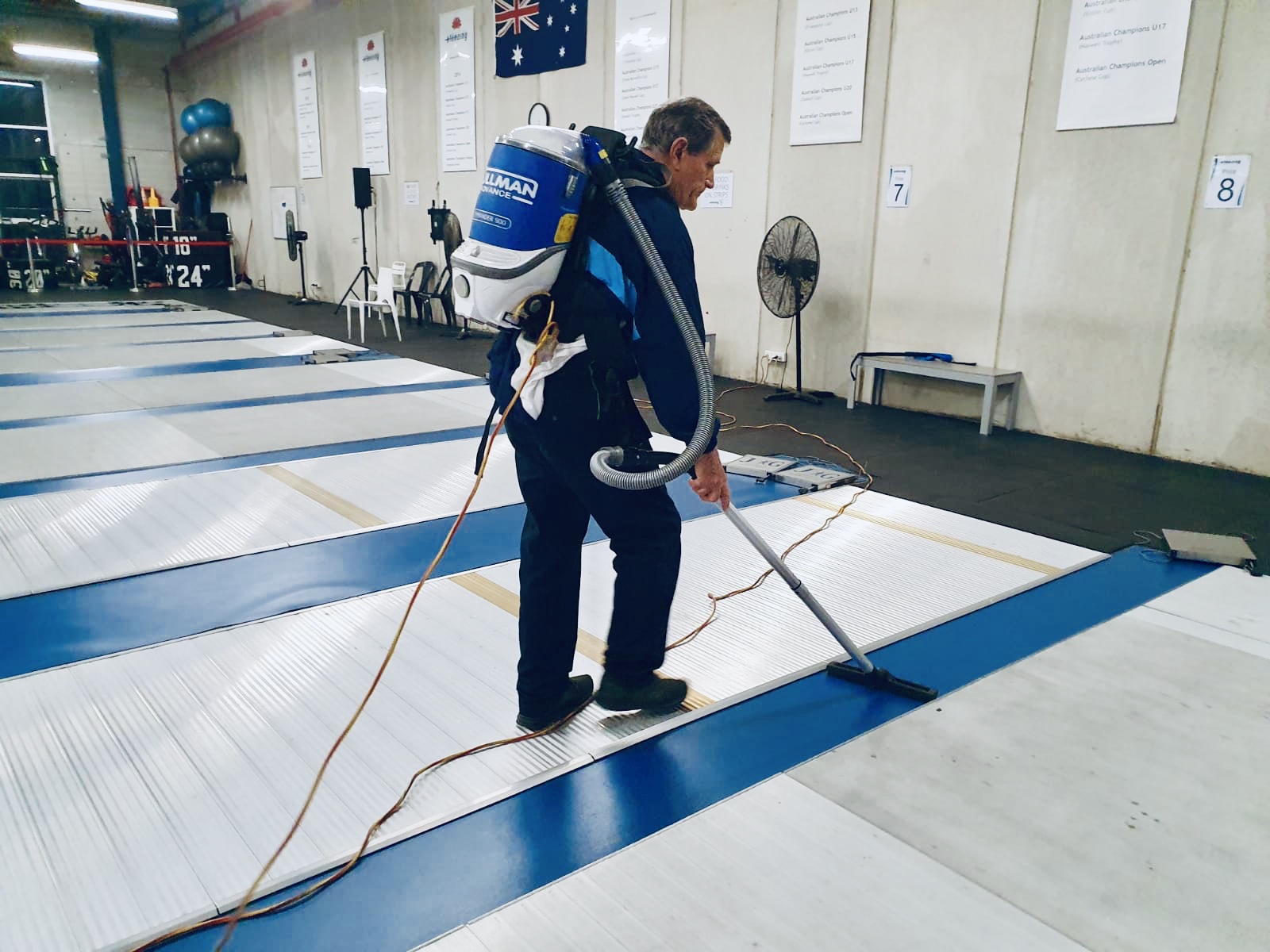 Man wearing vacuum cleaner on his back cleaning floor in a sport hall