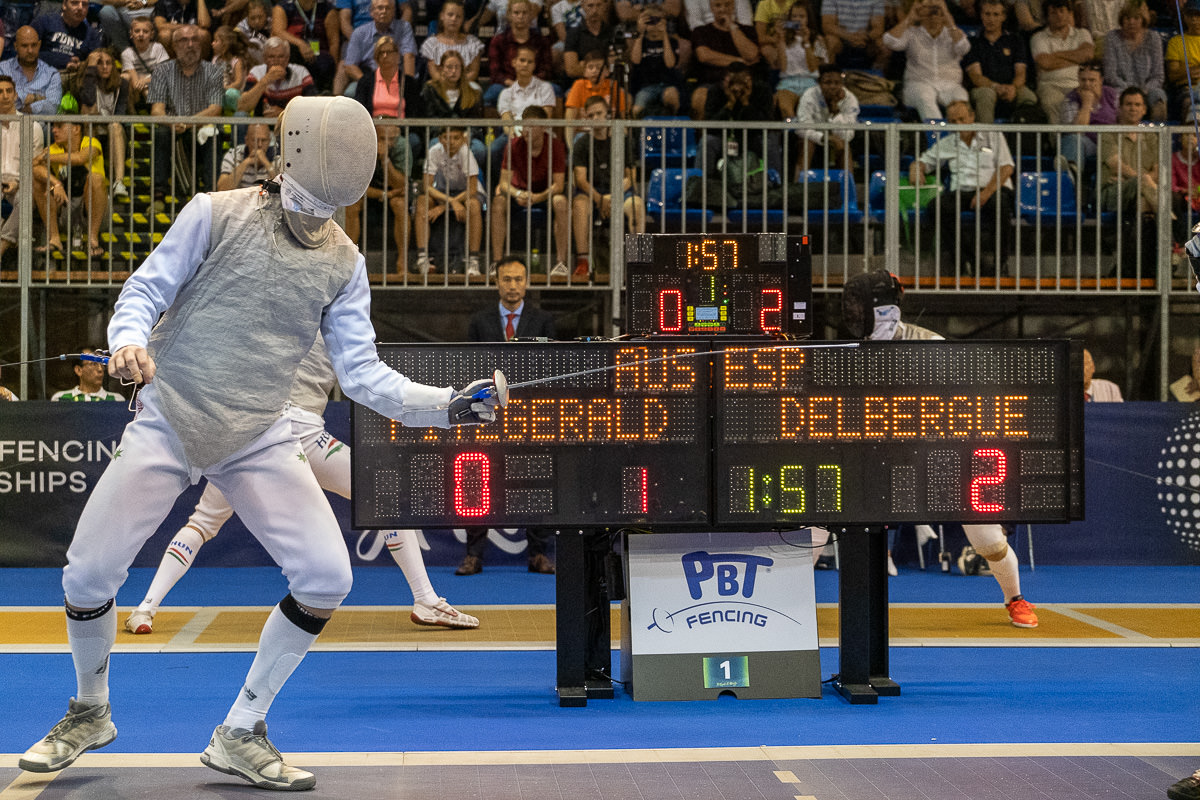 Man holding a sword competes in fencing with a crowd in background