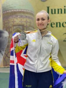 Woman wearing Australian Fencing tracksuit draped in an Australian flag holding a silver medal